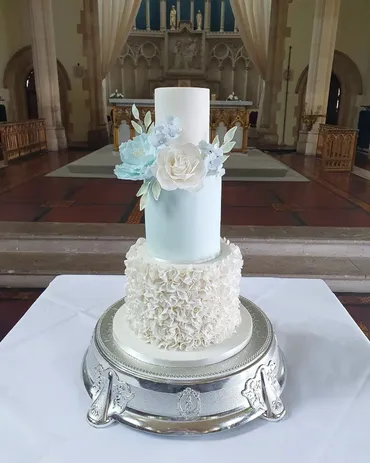 Three-tier white and blue wedding cake with gold monogram and sugar flowers